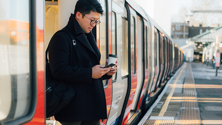 Man stepping out of train holding a coffee and looking at mobile phone