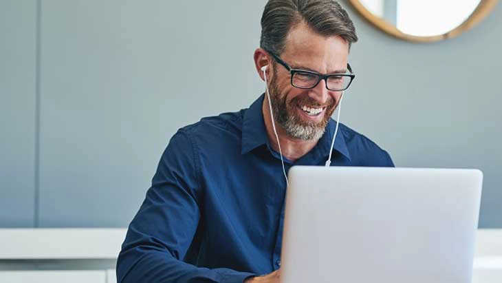 Man with glasses and wearing earphones working on lap top