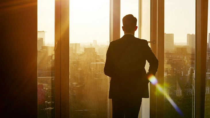 Man in suit looking out office window at city landscape