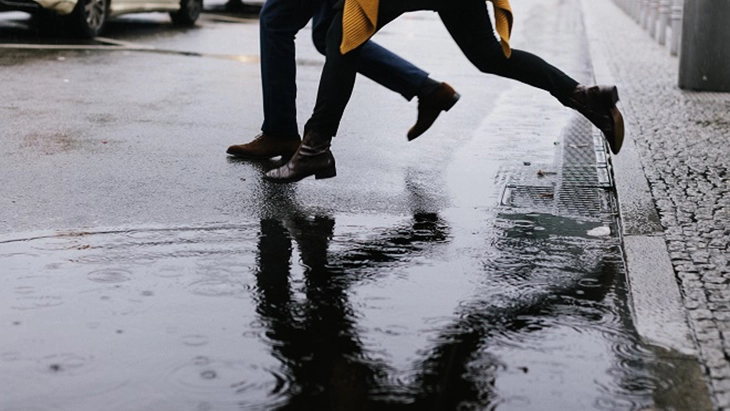 Two pair of legs, in black trousers and boots, running across rain-soaked street 