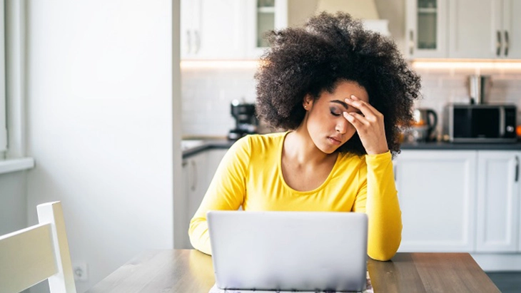 Woman working on laptop with head in her hand