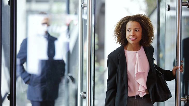 Young woman walking through interior glass door 