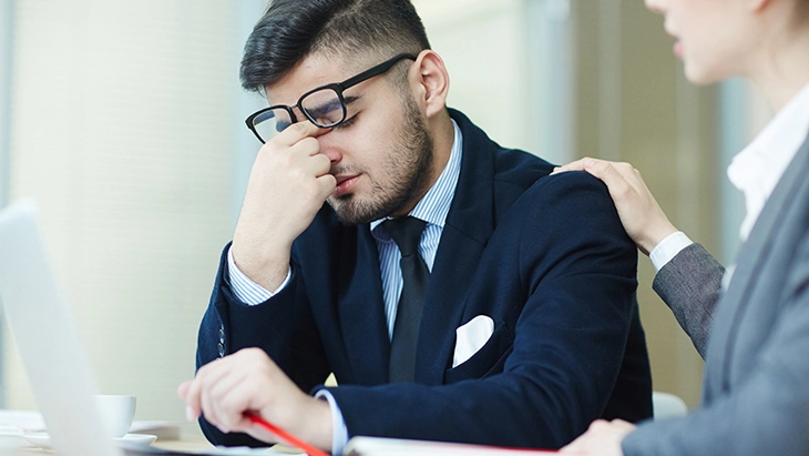 Man sitting at desk looking down with head in hand