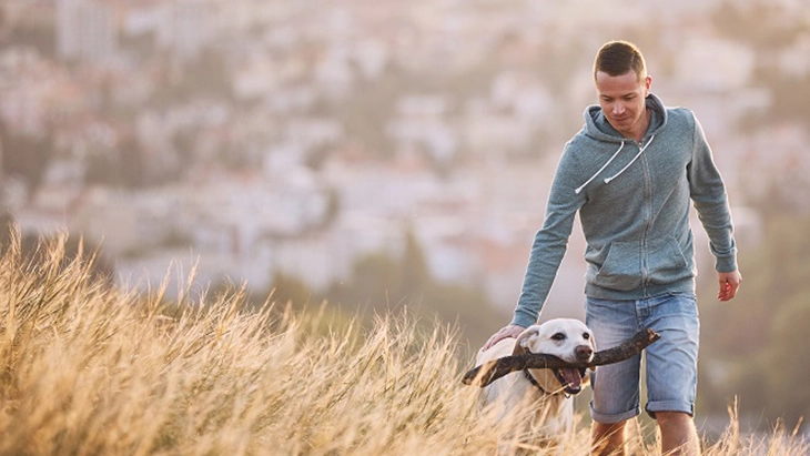 Man walking with dog through field of tall grass