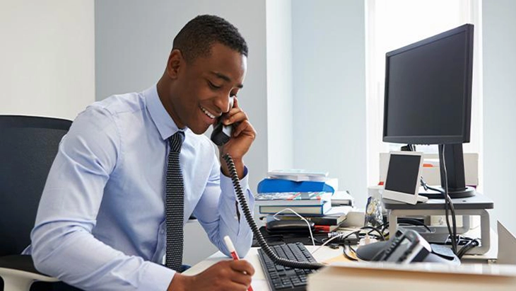 Young man sitting at work desk and talking on phone